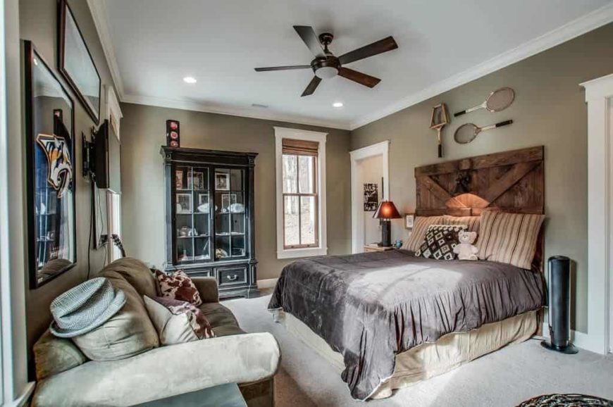 Primary bedroom featuring gray walls and carpet flooring, along with multiple wall decors. The room has a nice bed, a classy large couch and a freestanding shelf.