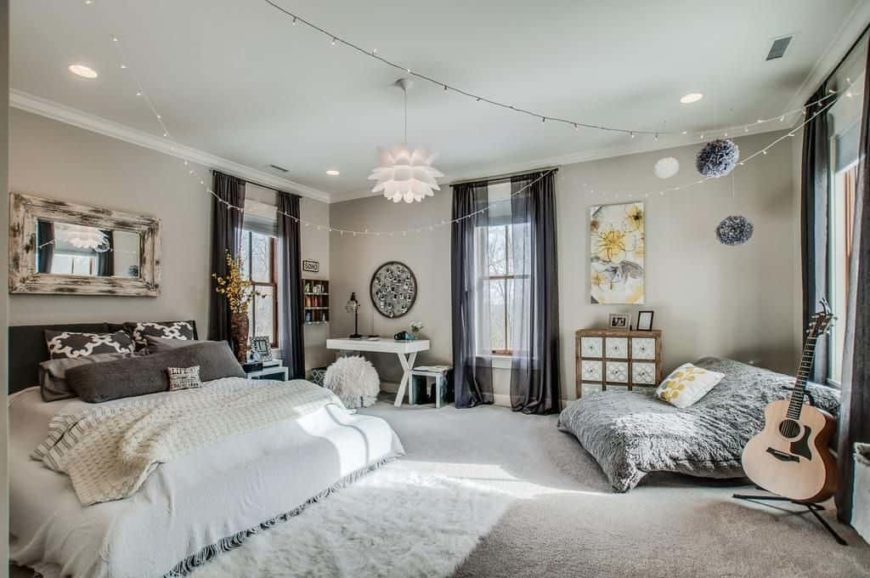 Large primary bedroom with gray walls and gray carpet flooring. There's a large comfy bed and a nice lounging couch on the side, along with a small study desk in the corner.