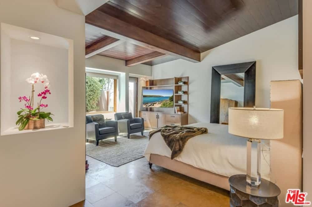 Side view of the bedroom showing an inset wall niche filled with gorgeous flowers along with gray armchairs by the picture window that invites natural light in.