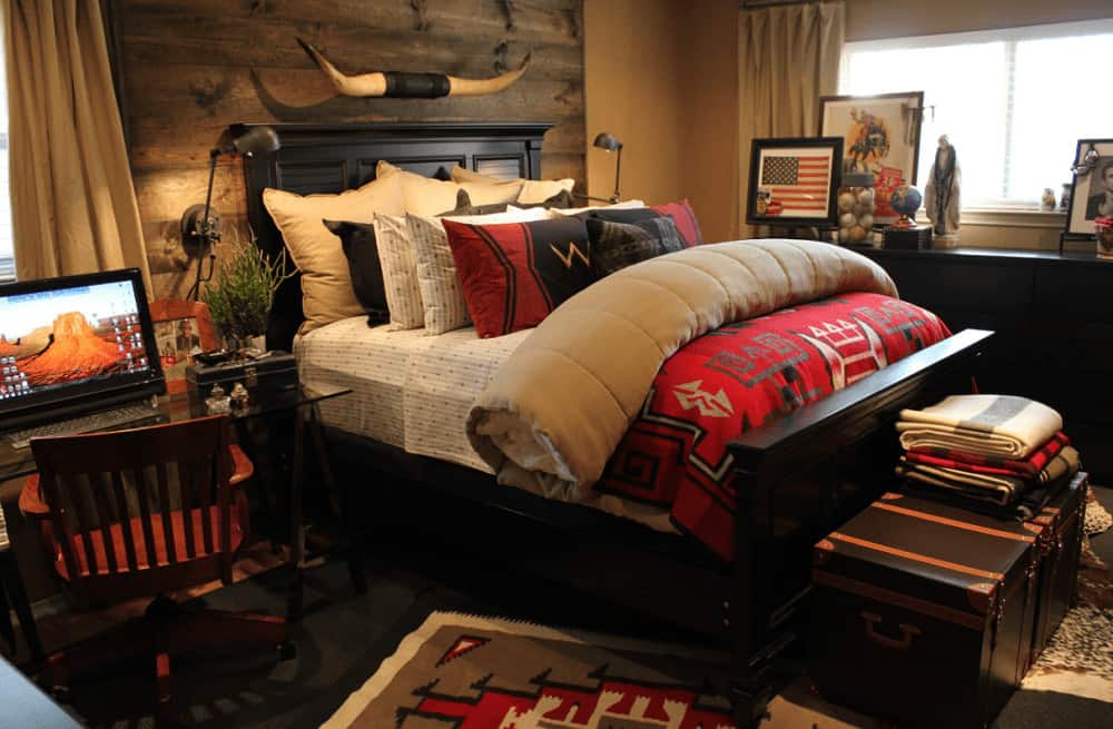 Southwestern bedroom offers a glass top desk paired with a wooden chair along with a black bed designed with a horn decor that's mounted on the wood plank accent wall.