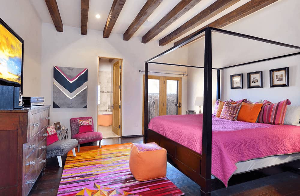 This bedroom boasts a canopy bed and a striking striped rug that lays on the wide plank flooring. There's a seating area beside the wooden cabinet that's fitted with glass knobs.