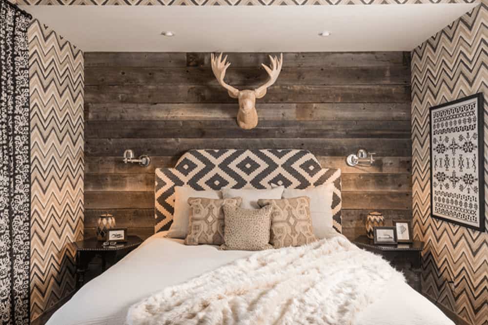 Clad in chevron wallpaper and rustic wood plank, this primary bedroom boasts a deer head decor and comfy bed flanked by hexagonal nightstands and chrome sconces.
