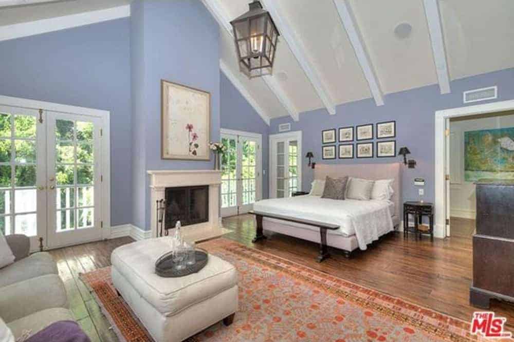 A lantern pendant light illuminates this blue bedroom offering a fireplace and a seating area that faces the bed accented with gallery frames.