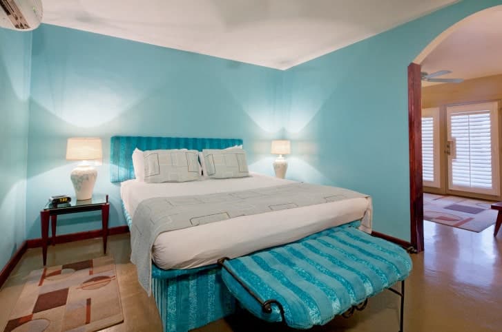 A black metal cushioned bench matches the blue striped bed in this sky blue bedroom illuminated by white table lamps that sit on wooden nightstands.