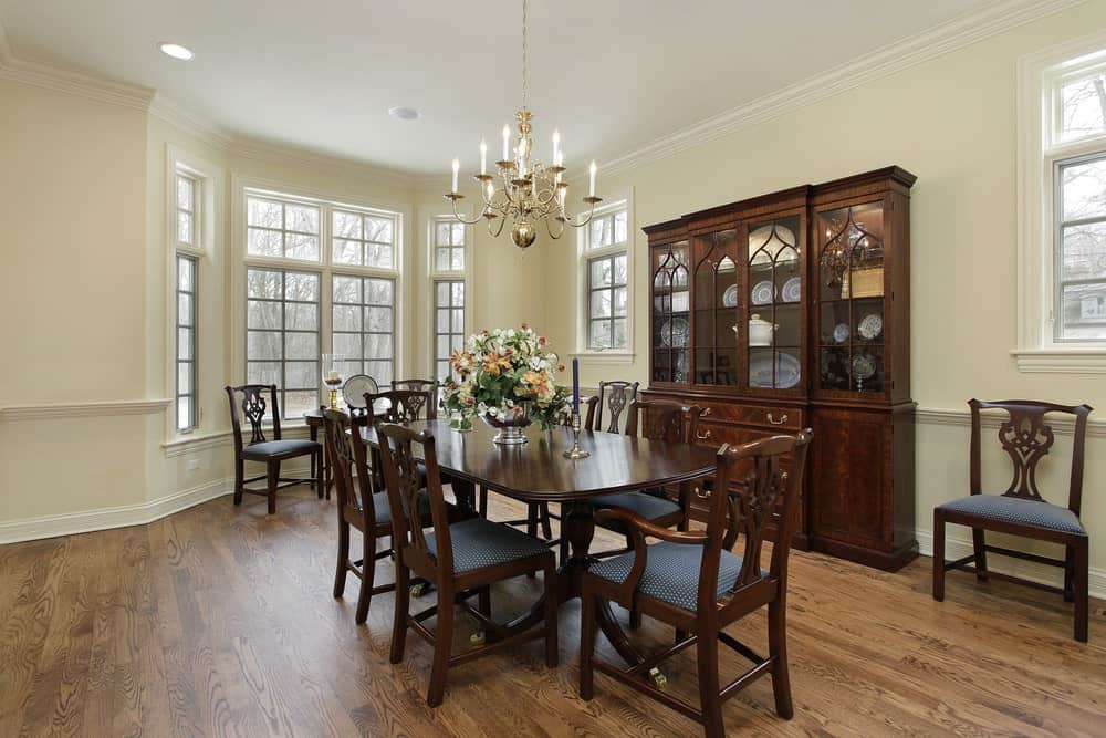 There is a close interaction between the hardwood flooring and dark brown hue of the wooden dining set that matches with the dining room cabinet and the chairs. This is then contrasted by the light beige walls and white ceiling.