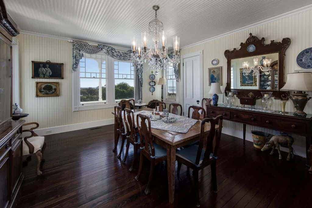 The white ceiling of this country-style dining room matches with the beige walls with the same textured finish. These light hues are contrasted by the dark brown hues of the dining set, the wall-mounted mirror and the hardwood flooring.