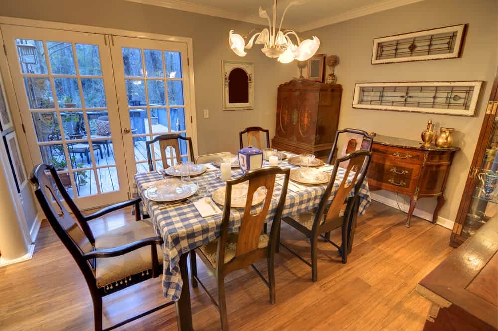 The blue checkered table cloth of this country-style dining room matches with the French glass doors with blue tinted glass. The blue elements are augmented by the warm yellow lights of the lovely chandelier that looks like flowers.