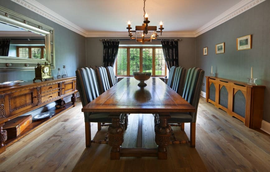This country-style dining room has a certain warmth to its hardwood flooring that complements the wooden dining table and the two wooden cabinets that stand out against the gray walls that match with the cushions of the dining chairs.