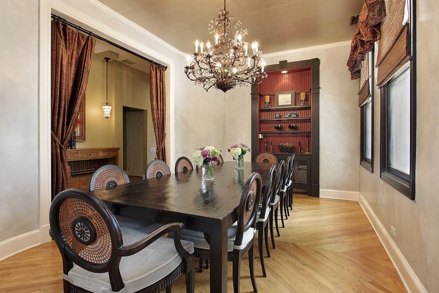 The long rectangular wooden dining table has a dark brown hue that matches with the cabinet that is embedded into the light gray wall. It has a dark wooden frame that complements the light hardwood flooring and ceiling.