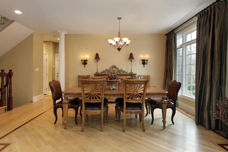 The two dining chairs at each end of the dining table has brown leather cushion while the rest are wooden with a carved back with a sun-like design. This is a complement for the light hardwood flooring as well as the white ceiling that hangs a chandelier over the table.