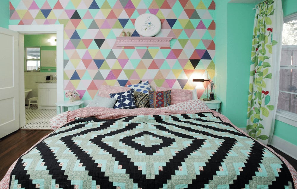 A multi-color patterned wall adds a striking accent in this charming bedroom with a comfy bed and pink floating shelf topped with mini sculptures and round wall art.