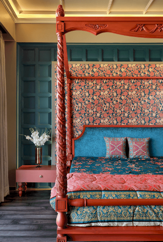 Sophisticated bedroom features a canopy bed paired with a red nightstand. It has wide plank flooring and paneled walls accented with a floral backdrop.