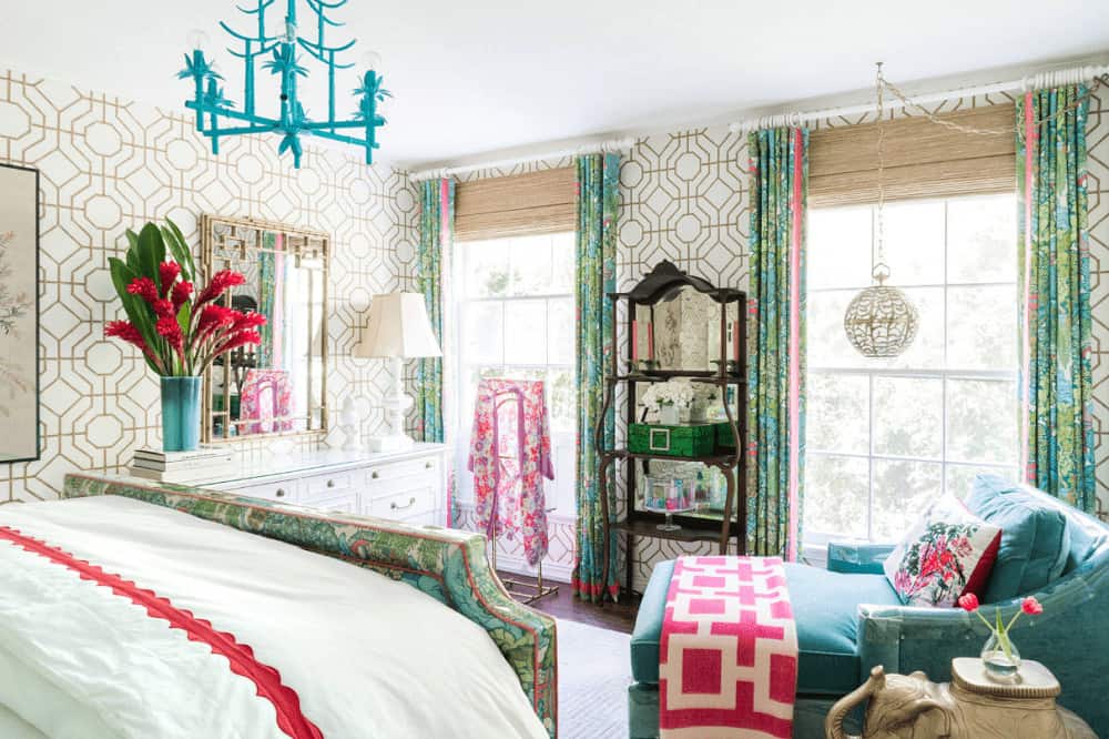 Gorgeous bedroom clad in patterned wallpaper that's accented with a stylish mirror. It is illuminated by a spherical pendant light and a unique blue chandelier that hung over the green printed bed matching with the draperies.