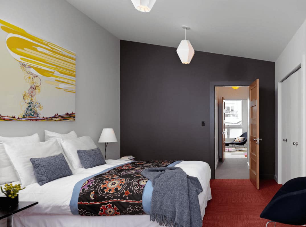 This primary bedroom is decorated with white geometric pendants and lovely painting that hung above the white skirted bed accented with a black patterned coverlet.