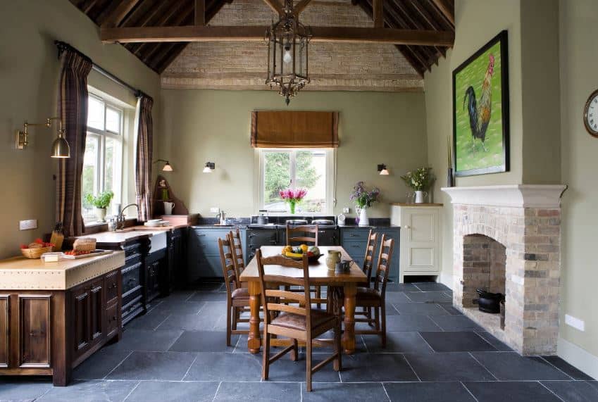 This informal country-style dining set is in the space created by the L-shaped peninsula of the kitchen beside the fireplace that is inlaid with stone bricks. This is contrasted by the blue tone of the stone floor that matches with the cabinetry of the kitchen.