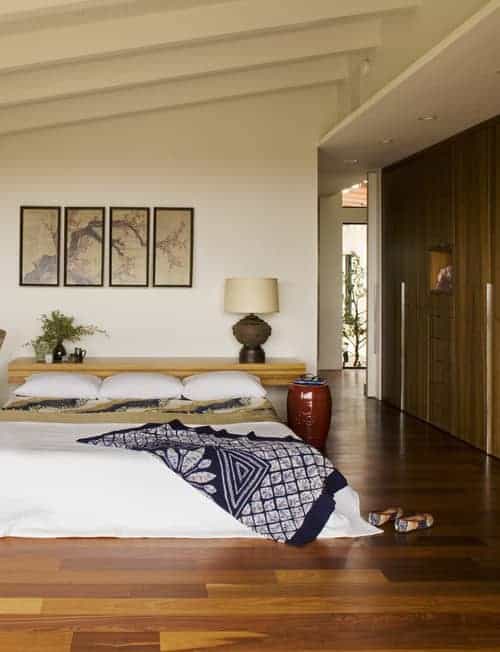 This bedroom is decorated with a gorgeous multi-panel wall art mounted above the floating shelf and low platform bed that's wrapped in a white blanket.