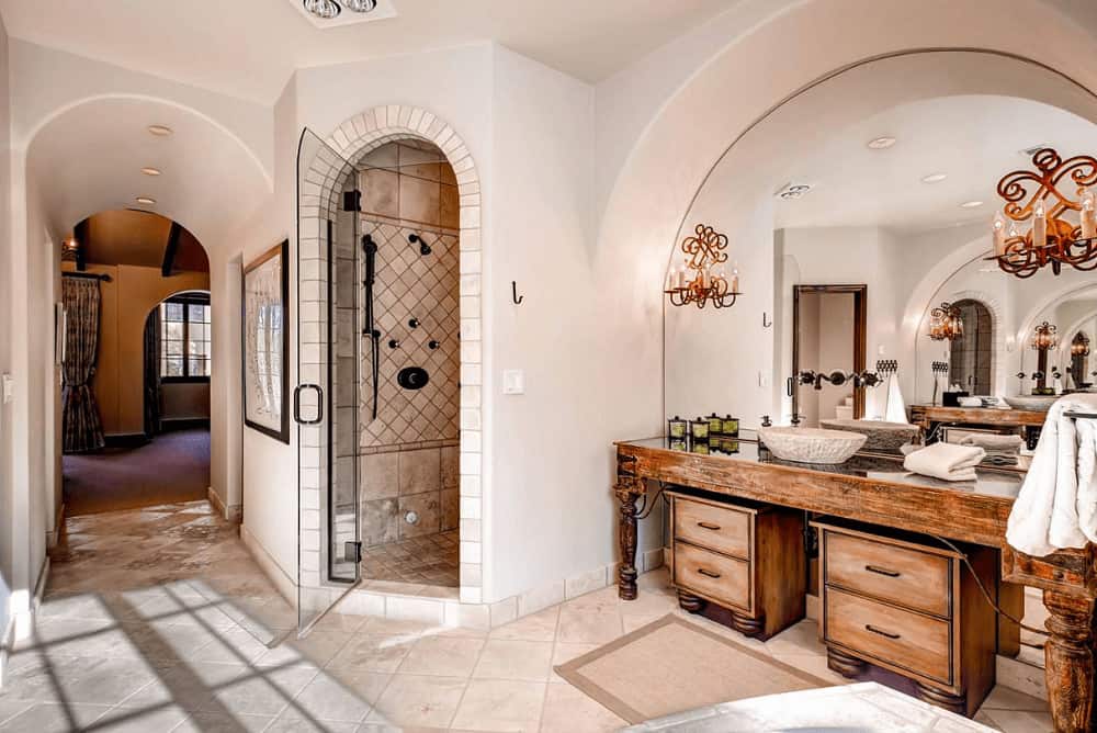 This primary bathroom showcases a walk-in shower and natural wood vessel sink vanity with an arched mirror mounted with beautiful candle sconces.