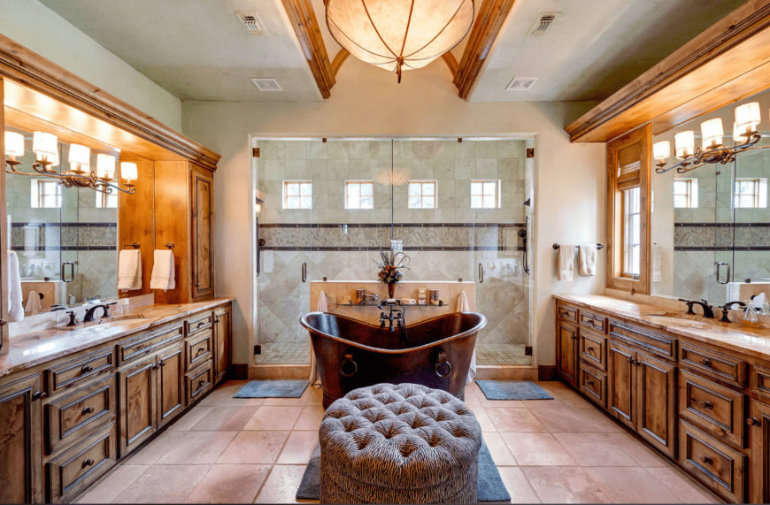 The beige primary bathroom features his and her sink vanity along with a walk-in shower and copper freestanding tub accompanied by a round tufted ottoman.