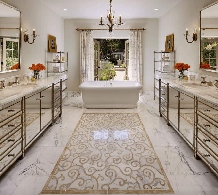 Fabulous primary bathroom with mirrored vanities and freestanding tub flanked by shelving units. It has white marble flooring designed with a lovely centerpiece along with a French door that opens to the yard.