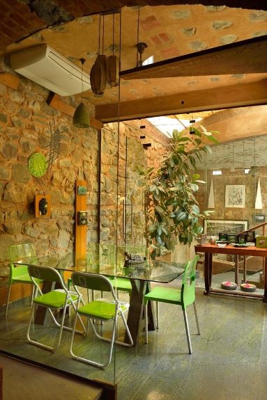 This is a nice fusion of Tropical-style elements and industrial-style elements. It has a tall textured stone wall paired with an arched brick ceiling and a gray concrete flooring. These elements makes the green modern chairs stand out as well as the green wall clock and potted plant.