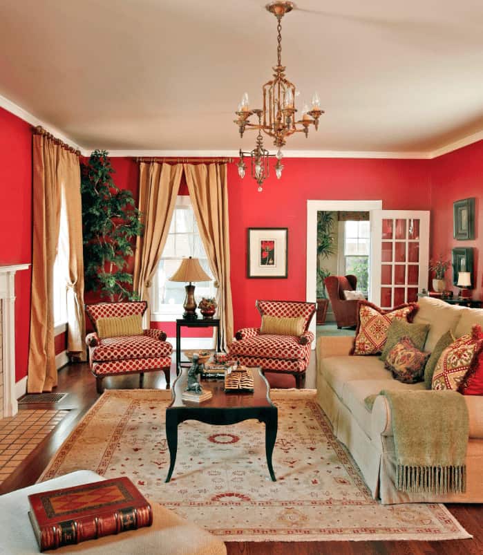 A skirted sofa faces the black coffee table in this living room with red patterned wingback chairs and a floral rug that lays on the rich hardwood flooring.