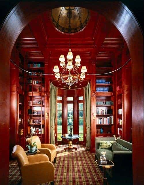 A view of the redwood living room from the arched doorway showcasing cozy seats and glass top side tables over patterned carpet flooring. It includes built-in bookshelves and a fabulous chandelier that hung from the coffered ceiling.
