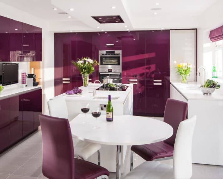 This kitchen has an informal dining area beside it that has a modern white round table and purple leather chairs. This matches well with the modern sleek cabinets of the kitchen that stands out against the white ceiling and counters.