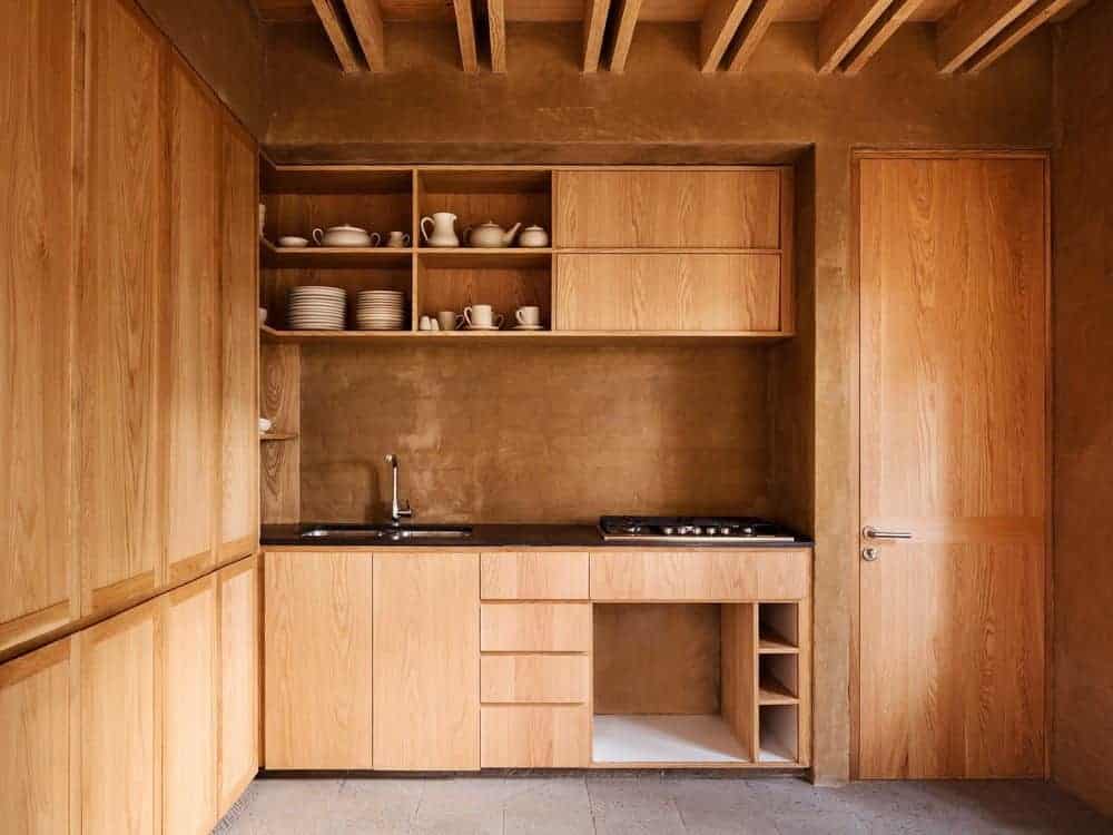 Brown kitchen with a unified look featuring a black granite countertop and wooden cabinets that blend in with the walls and ceiling. It includes a cooktop and an undermount sink paired with a chrome faucet.