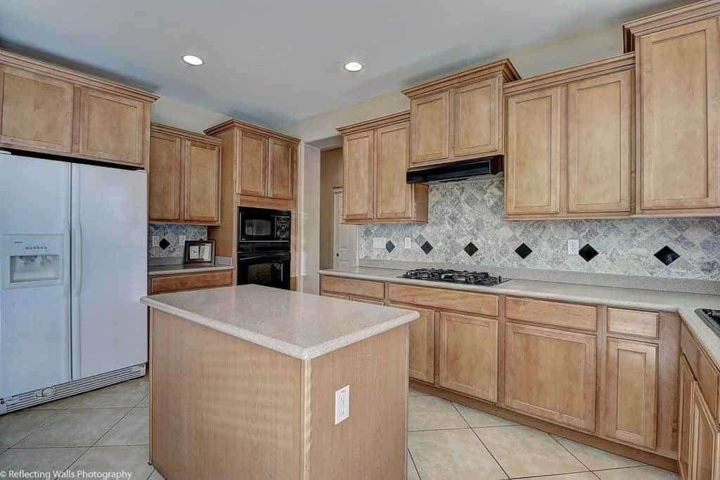 Diamond pattern backsplash adds a nice accent in this kitchen offering wooden cabinetry and a small island along with contrasting black and white appliances.