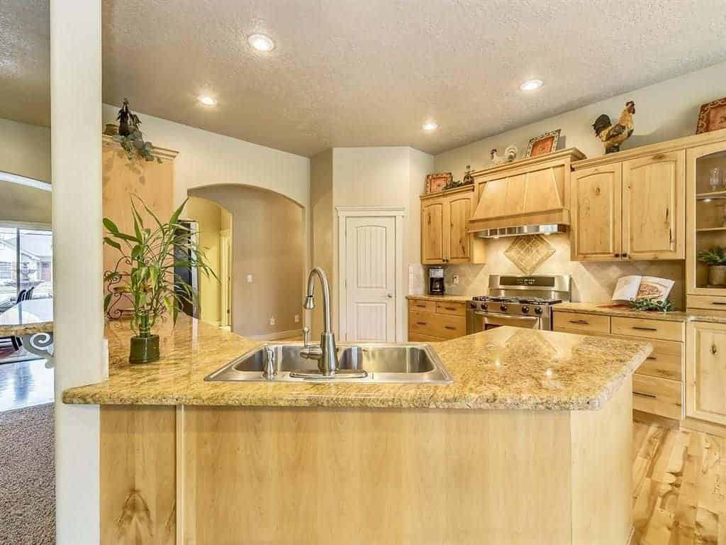 Warm kitchen with stainless steel appliances and natural wood cabinetry complementing with the hardwood flooring and peninsula that's topped with a granite counter and sink.