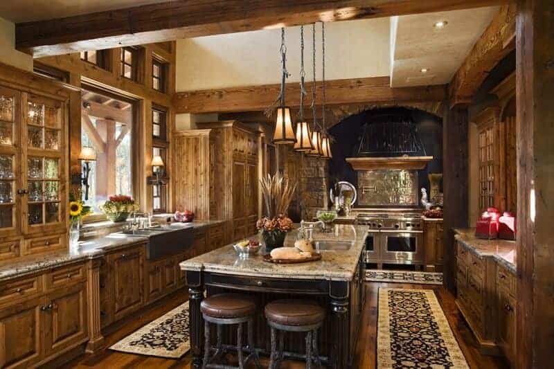 Rustic kitchen showcases an arched cooking alcove and wooden cabinetry that blends in with the hardwood flooring topped with black floral runners. There's a granite top island in the middle paired with round barstools.