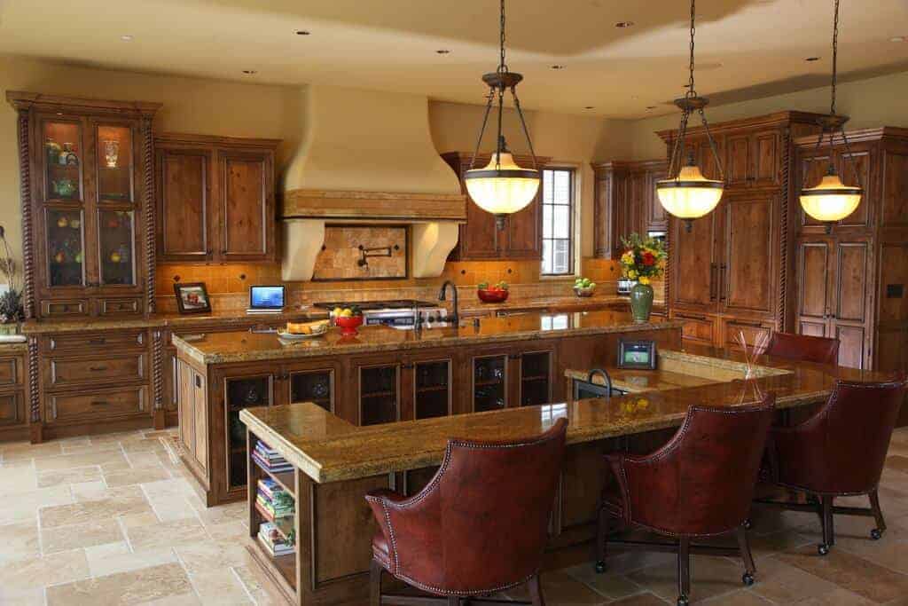 Glass pendant lights hang over the breakfast bar that's lined with brown leather chairs. It is attached to a granite top island matching with the wooden cabinetry against the yellow walls.
