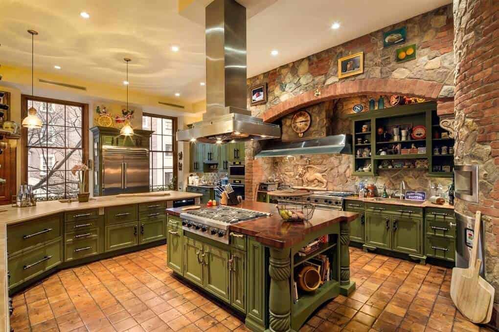 Marvelous stone walls add texture in this kitchen with green cabinets and peninsula matching with the island bar under a sleek range hood. It has tiled flooring and regular white ceiling mounted with recessed lights and glass dome pendants.