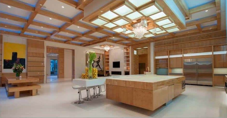 Modern kitchen illuminated by stunning light fixtures mounted on the drop ceiling that is suspended over an immense island. It is attached with a long sleek bar paired with matching stools.