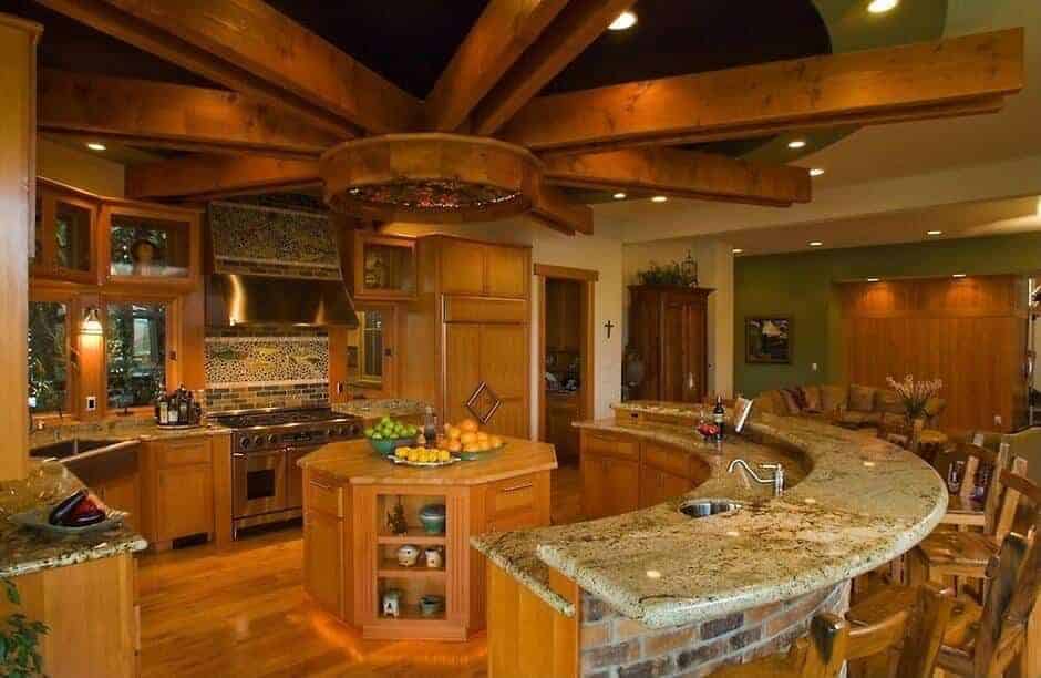 A semi-circular raised island along with stainless appliances and wooden cabinets surround an octagonal island that blends in with the rich hardwood flooring. It is situated under a marvelous round tray ceiling that's lined with wood beams arranged in a sunburst pattern.