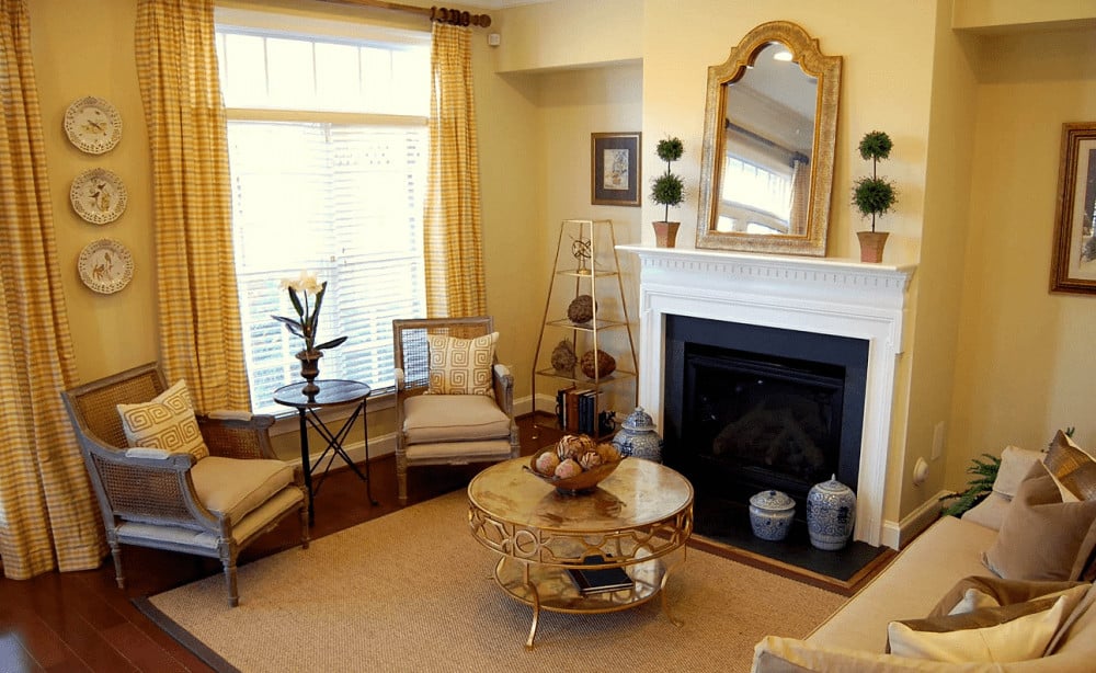 A brass shelving unit complements the stylish coffee table surrounded by cushioned seats and a fireplace topped with an arched mirror and potted plants.
