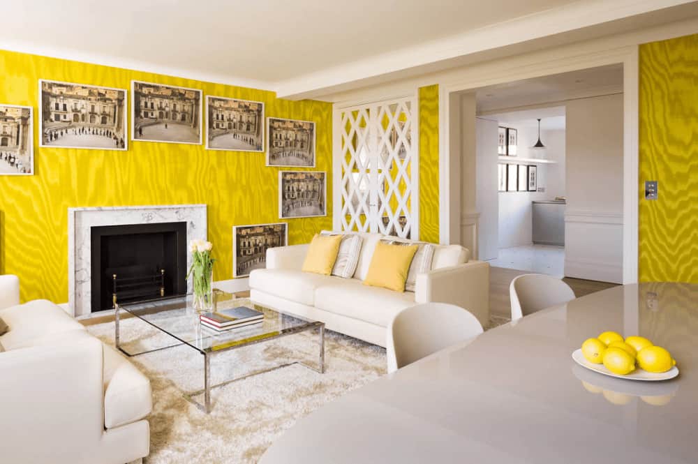 Clad in yellow wavy wallpaper, this living room boasts facing sofas and a glass top coffee table across the fireplace surrounded by framed pictures.