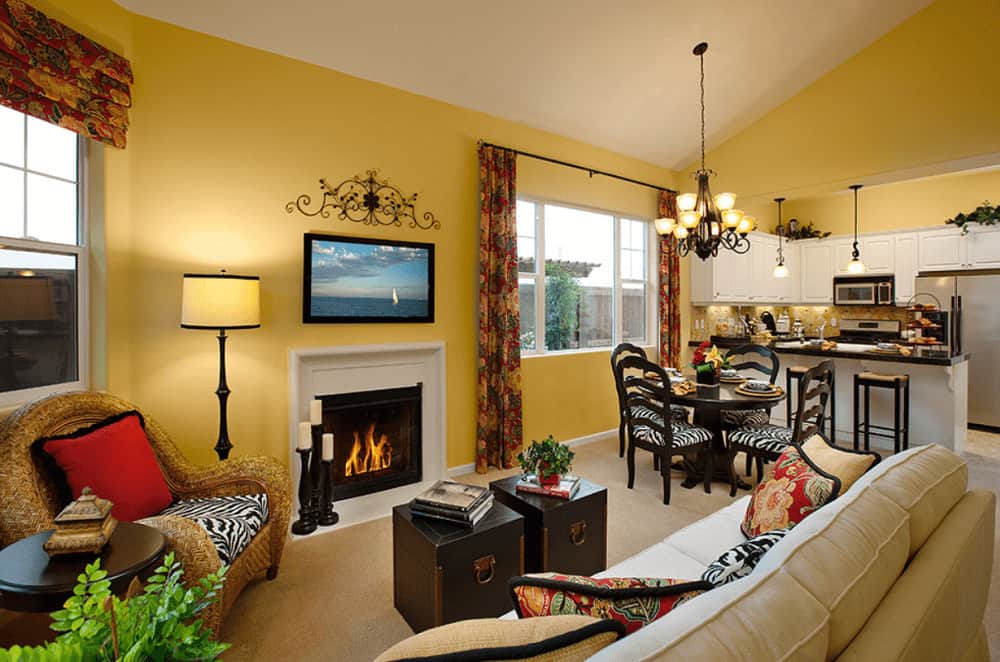 A modern fireplace faces the dark wood coffee tables and beige sectional sofa filled with fluffy pillows. It is accompanied by a wicker chair and a drum floor lamp.