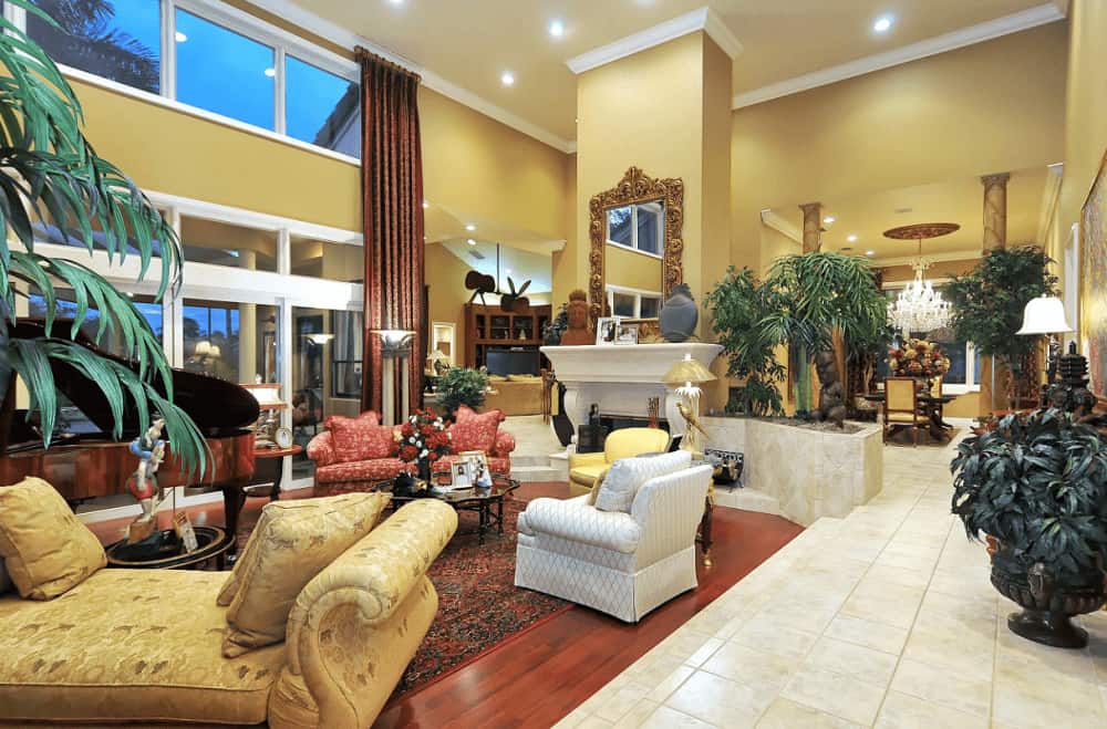 Green potted plants create a refreshing ambiance in this elegant living room showcasing classy seats and a fireplace with ornate mirror on top.