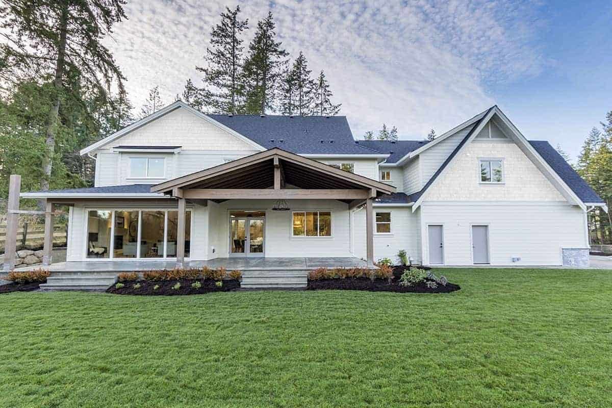 This view of the house offers a closer look at the wide well-manicured lawn of grass in the backyard. There are also some shrubs planted by the stone steps leading to the house that has large sliding glass doors on the side leading to the living room.
