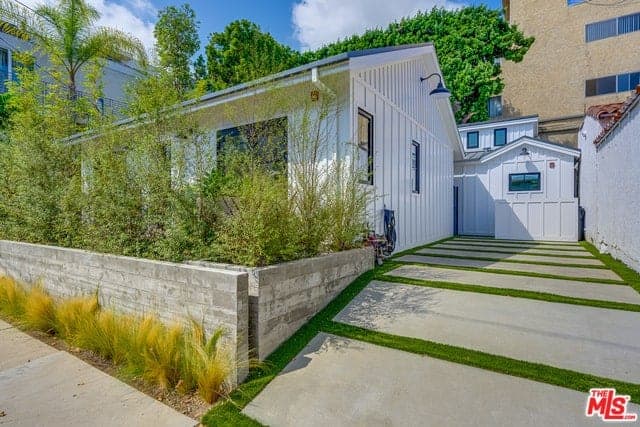 The driveway at the side of the white exterior walls has concrete blocks with carpets of grass in between to emphasize the lines. Beside this is a low concrete wall that doubles as a planter for the tall shrubs that provide privacy for the home and acts as a live fence as well.