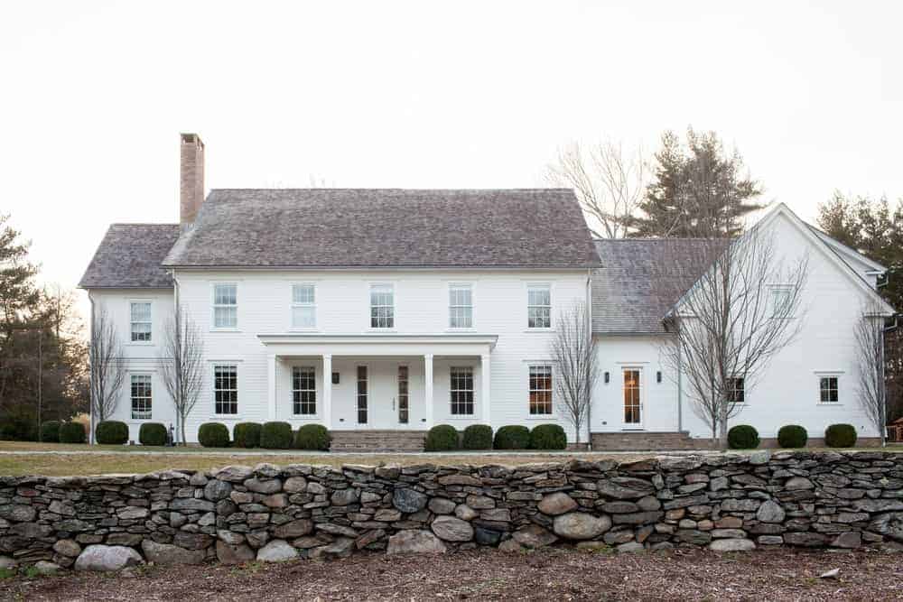 The large property is surrounded by a low wall of various-sized stones creating a charming and rustic foreground for the lawns of grass and the circular shrubs that line the walls of the house outside and also flanks the steps to the entry way.