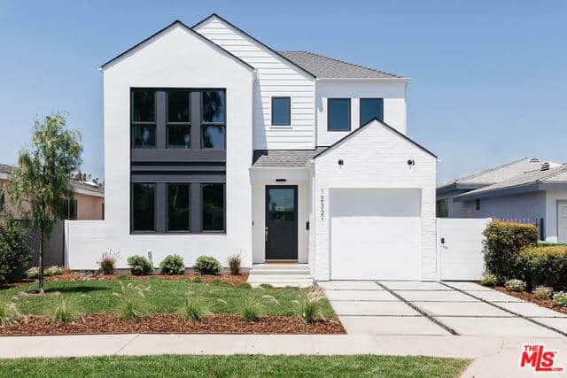 The bright white exterior walls of this home is complemented by the bleached concrete driveway leading to a stark white garage door. The brightness of these elements are somewhat counterbalanced by the front lawn that has grass and shrubs arranged in a manner that showcases the soil.