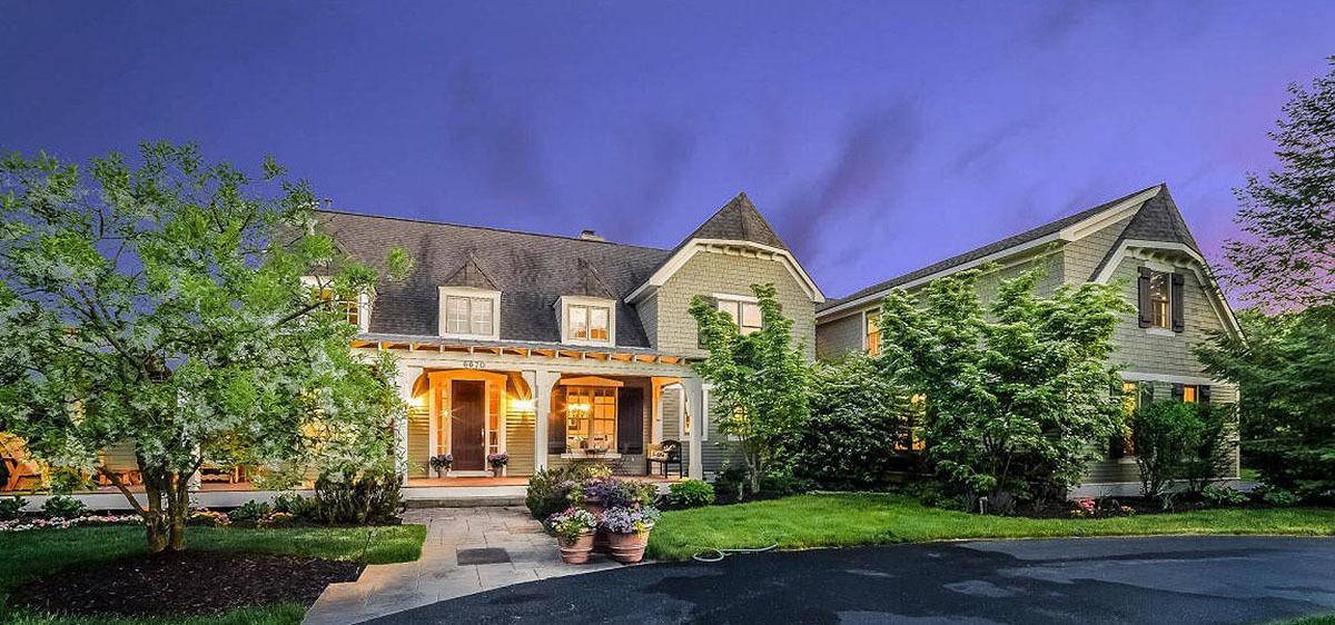 This is a front yard view of the house that has multiple tall trees providing a nice complement to the gray exteriors. These are matched with a gray concrete walkway with potted flowers on one side and a couple of grass carpets separating the property from the asphalt road.