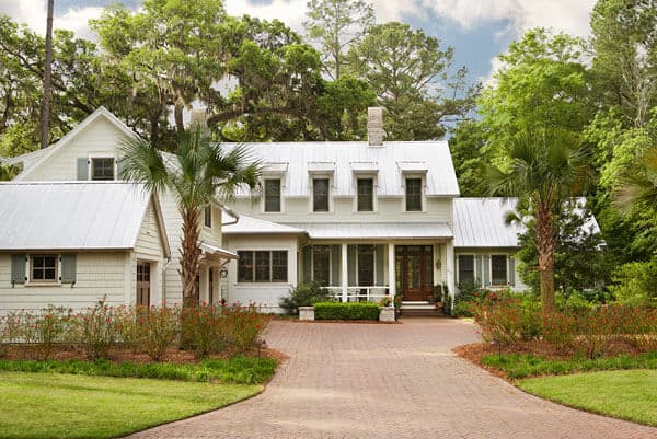This home has a terracotta wide walkway and driveway that is flanked by carpets of green grass complemented by the flowering shrubs and a couple of tropical trees standing guard on each side of the entrance standing out against the white exteriors.
