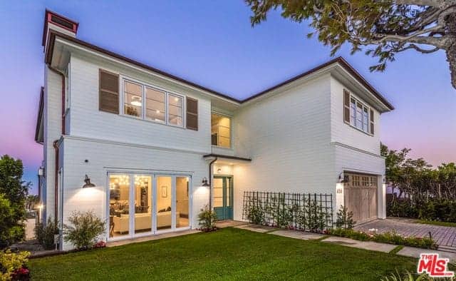 The white exterior walls of this beautiful home provide a nice background for the lush green landscaping. The driveway on the far right matches with the walkway next to it that is lined with flowering shrubs and a vertical garden near the entryway that is lit with warm welcoming yellow lights.