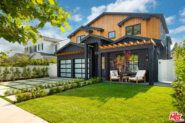 The black hue of the house exterior walls is an amazing dark background for the simple landscaping that has a driveway of concrete with green carpets of grass in between blocks. This matches well with the walkway and the lawn of grass on the far right.