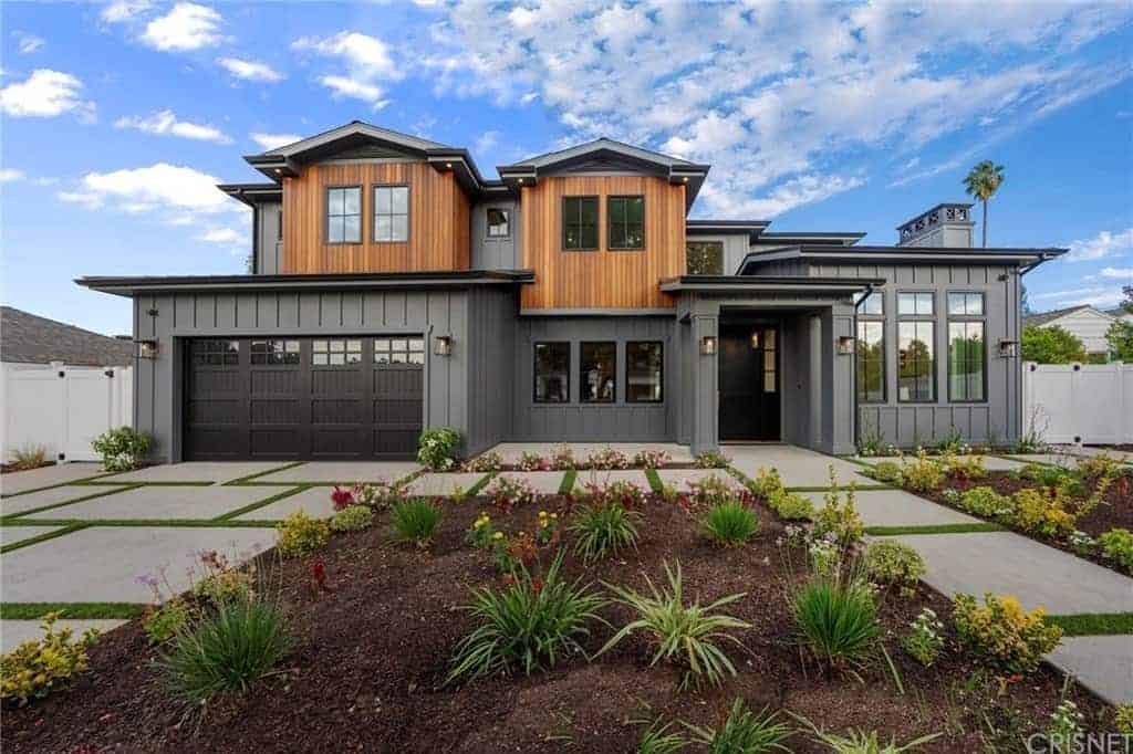 This brilliant home has a gray first floor that is complemented by the gray concrete walkways and driveway that both lead to a dark gray door flanked by wall-mounted lamps. This is accented with colorful spaced shrubs of the front lawn.