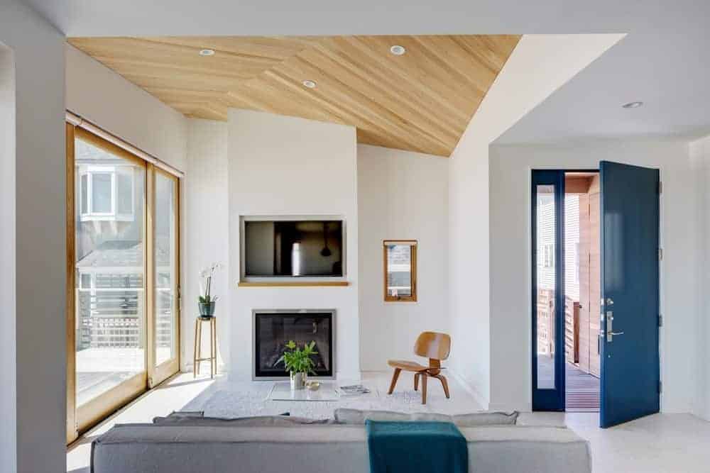 A blue door opens to this living room with a wooden chair and gray sofa paired with a glass coffee table. It includes a fireplace and TV fitted on the white pillar.