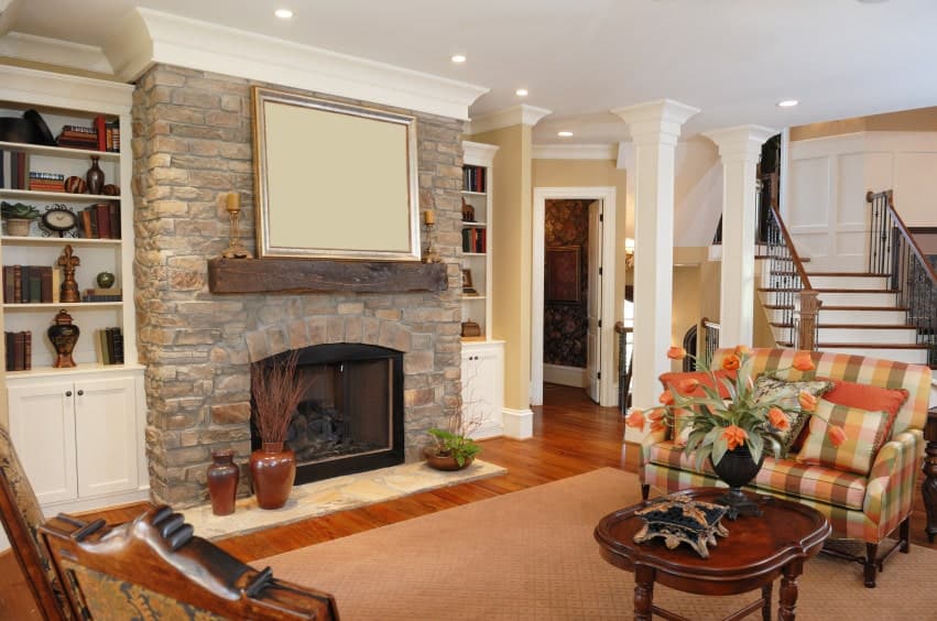 A brick fireplace lined with rustic mantel adds texture in this living room with a plaid sofa and a wooden coffee table topped with a flower vase.
